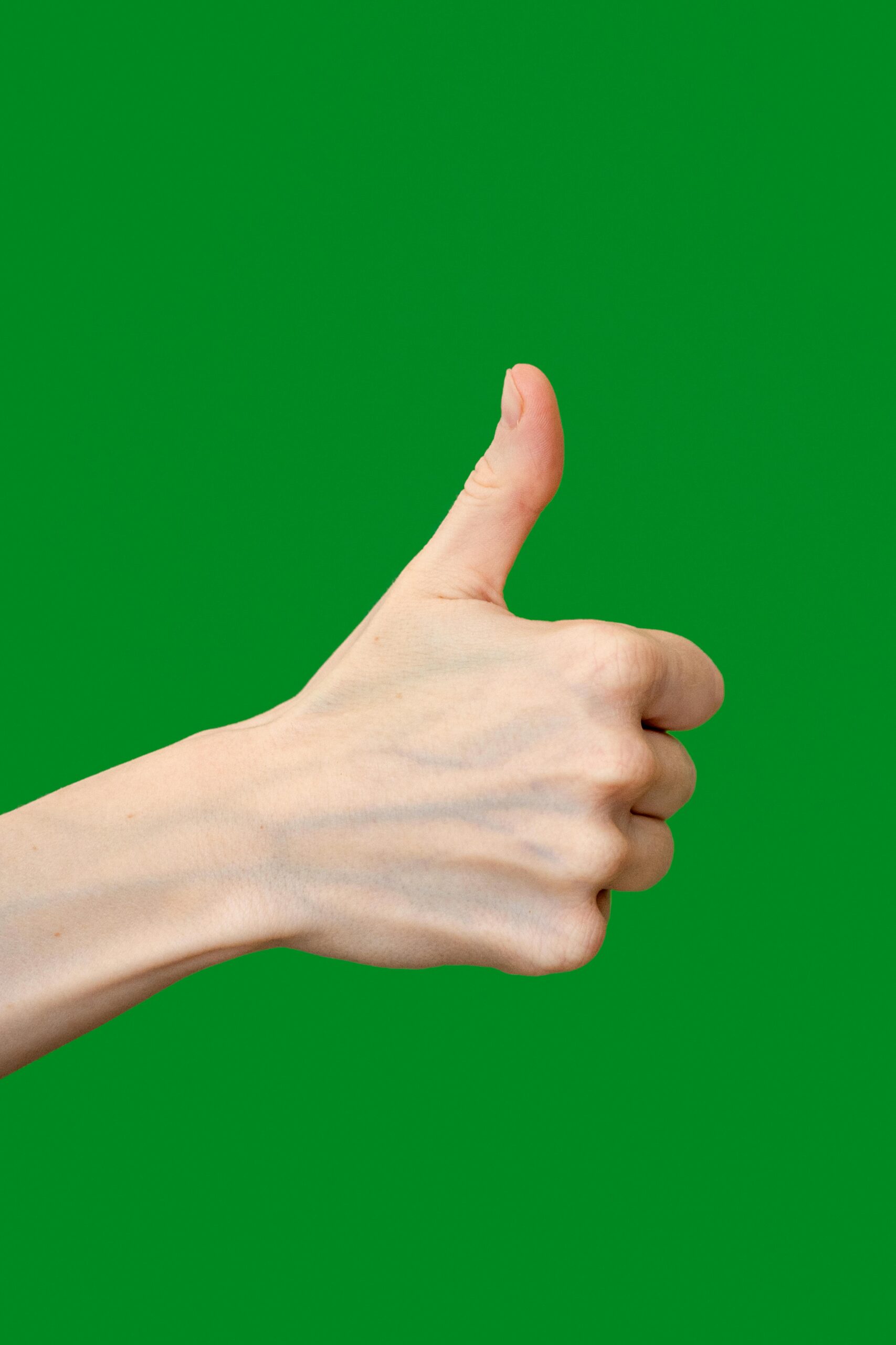 Close-up of a human hand showing a thumbs up sign against a green background.